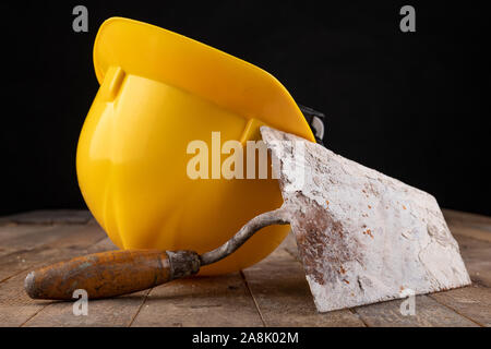 Protective helmet and tools for bricklayer. Work accessories for production workers. Dark background. Stock Photo