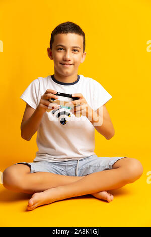 Child using video game Controller. Kid with Joystick playing Computer Game on yellow background Stock Photo