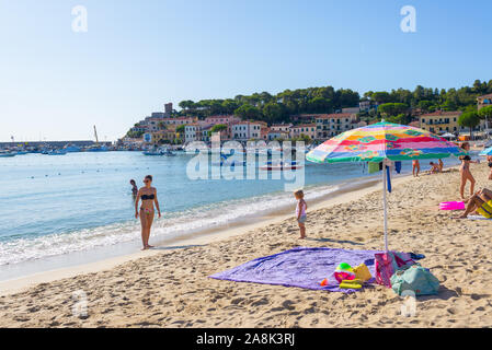 Marina di Campo, Isola d'Elba, Italy - September 2019: People on the beach in Marina di Campo with harbour and village in the background Stock Photo