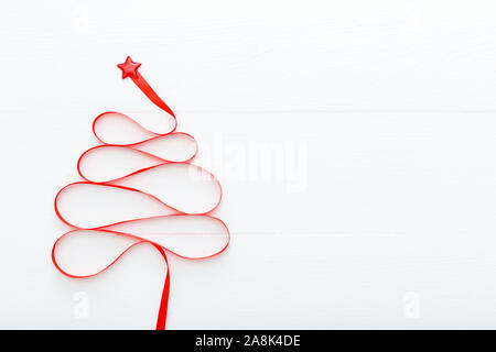 Christmas Tree made from Red satin ribbon with a star on the top on white wooden background. Xmas, winter, new year concept. Flat lay, top view, copy