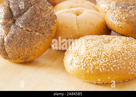 Assortment of kaiser roll breads. There are plain ones, some with sesame seeds and the other have poppy seeds. Focus on the foreground. Stock Photo