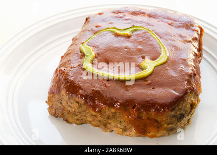 homemade fresh baked meat loaf topped with a slice of green bell pepper and a ketchup based sauce. This delicious meal is served on a white plate. Stock Photo