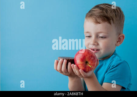 Portrait happy, smiling boy choosing junk food. Healthy versus unhealthy food. Healthy vs unhealthy eating, teenager choosing between cookie or an app Stock Photo