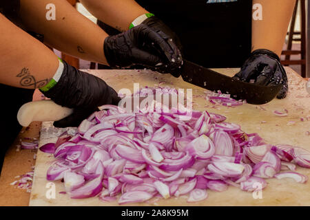 two pair of hands cutting onions on a wooden table with knifes Stock Photo