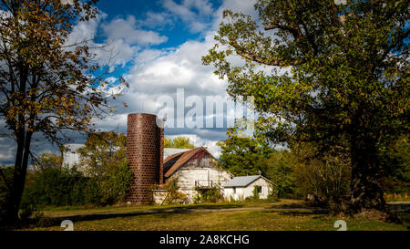 White barn and silo framed by two  trees in the fall in rural North Carolina Stock Photo