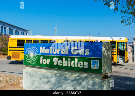 Natural gas school bus fueling behind natural gas for vehicles sign at compressed natural gas CNG fueling station byPacific Gas and Electric Company Stock Photo