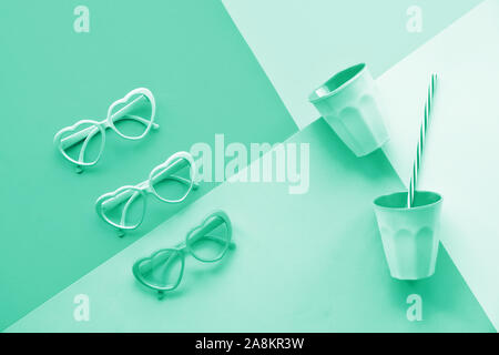 Monochrome color image toned biscay green. Split paper background, geometric flat lay, top view on heart shaped glasses and shiny plastic drinking gla Stock Photo