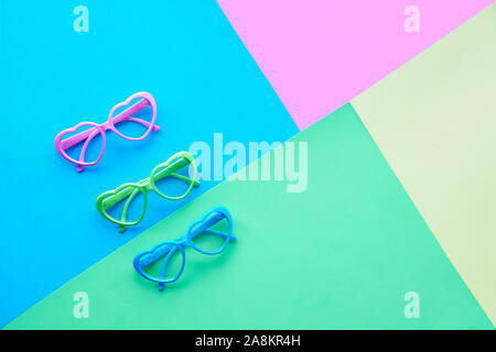 Multicolored paper background in pastel colors, flat lay, top view on three pairs of heart shaped glasses or sunglasses, geometric diagonal creative f Stock Photo