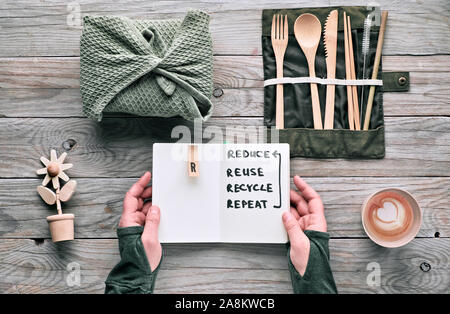 Flat lay, zero waste packed lunch with wooden utensils, cutlery, lunch box in textile, coffee in reusable cup. Sustainable lifestyle, hands hold noteb Stock Photo