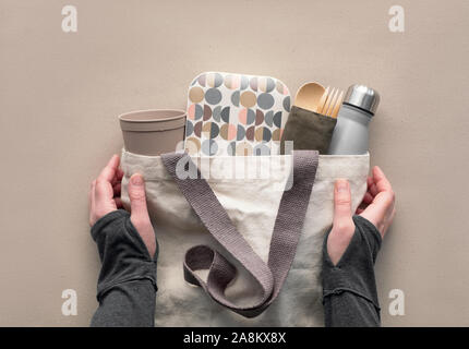Creative top view, zero waste packed lunch kit in canvas bag. Hands holding bag with takeaway lunch box, bundle with bamboo cutlery, reusable box and Stock Photo