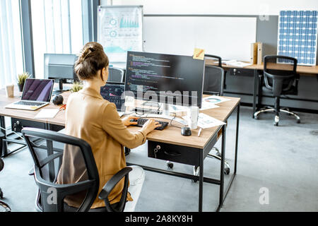 Young woman working as a programmer, writing programming code on the computer at the coworking space Stock Photo