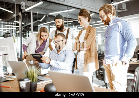 Senior manager having a meeting with office workers standing together near the working place in the modern office. Concept of a small conference and teamwork Stock Photo