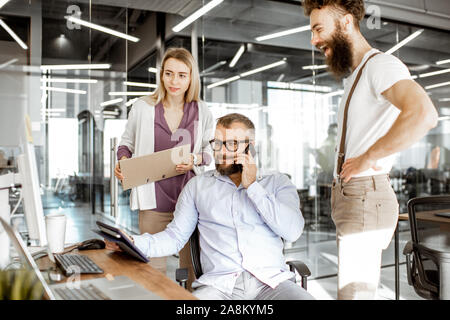 Senior manager having a meeting with office workers standing together near the working place in the modern office. Concept of a small conference and teamwork Stock Photo