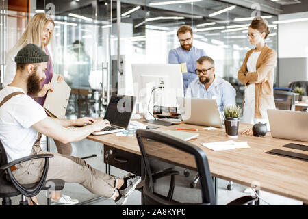 Group of diverse colleagues working on the computers in the modern office or coworking space, bearded hipster as a programmer writing code Stock Photo