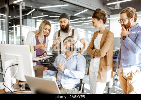 Senior manager having a meeting with office workers standing together near the working place in the modern office. Concept of a small conference and teamwork Stock Photo