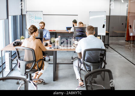 Group of diverse colleagues working on the computers in the modern office or coworking space, writing programming code Stock Photo