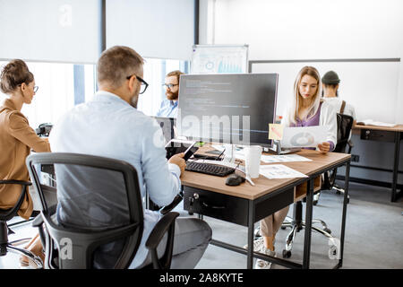 Group of diverse colleagues working on the computers in the modern office or coworking space, writing programming code Stock Photo