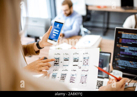 Developers or web designers developing mobile application for banking in the office, close-up on phone and paper sketches Stock Photo