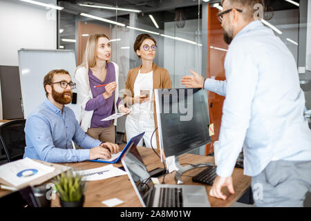 Group of diverse colleagues working in the modern office, having discussion or small conference on a working place with computers Stock Photo