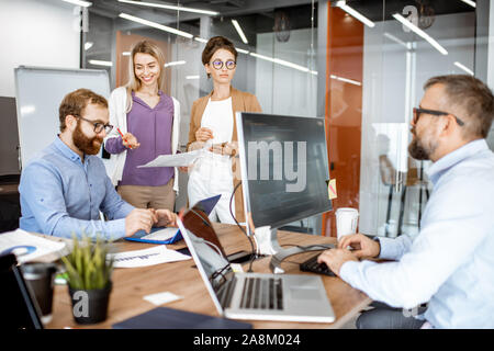 Group of diverse colleagues working in the modern office, having discussion or small conference on a working place with computers Stock Photo
