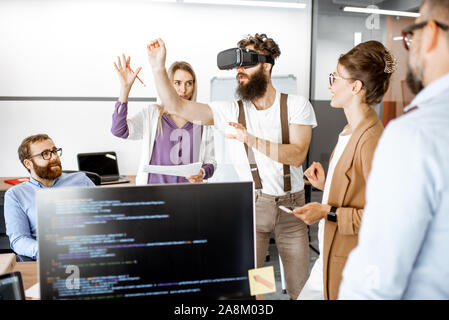 Group of diverse colleagues during small conference in the office, creative bearded man trying a new product with virtual reality goggles Stock Photo