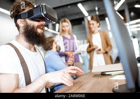 Young people working in the office, creative bearded man trying a new product or playing game with virtual reality goggles Stock Photo