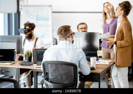 Group of diverse colleagues working with computers in the modern office or coworking space, writing programming code and working with vr goggles Stock Photo
