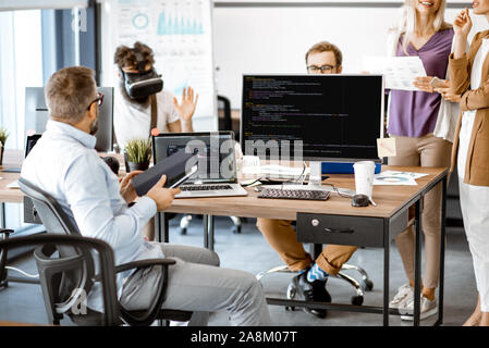 Group of diverse colleagues working with computers in the modern office or coworking space, writing programming code and working with vr goggles Stock Photo