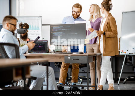Group of diverse colleagues working with computers in the modern office or coworking space, writing programming code and working with vr goggles Stock Photo