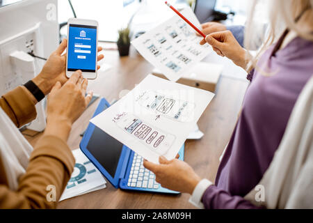 Developers or web designers developing mobile application for banking in the office, close-up on phone and paper sketches Stock Photo