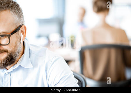Man with wireless earbuds in the office, close-up focused on earphones and cropped face Stock Photo