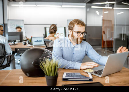 Young man dressed casually working on the laptop in the office with coworkers on the background Stock Photo