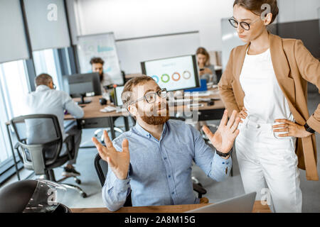Two young colleagues talking at the working place, solving some working moments in the busy office or coworking space Stock Photo