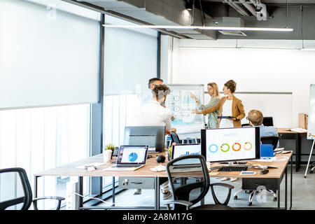 Group of diverse colleagues discussing some working momets with presentation on flipchart during a small conference in the office Stock Photo