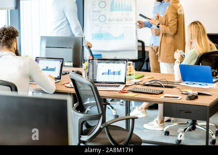 Man sitting on the working place with computers, thinking on some financial charts and graphs in the office with other coworkers Stock Photo