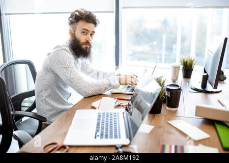 Portrait of a young bearded man at the working place with computer in the office Stock Photo