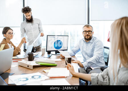 Group of diverse colleagues working in the modern office, having discussion or small conference on a working place with computers Stock Photo