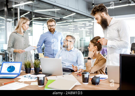 Group of diverse colleagues working in the office, having discussion or small conference on a working place with computers and printed documents Stock Photo