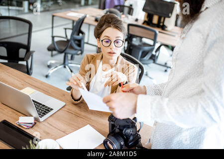 Two young colleagues talking at the working place, solving some working moments in the office or coworking space Stock Photo
