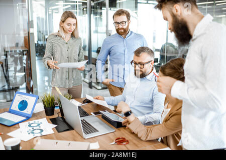 Group of diverse colleagues working in the office, having discussion or small conference on a working place with computers and printed documents Stock Photo