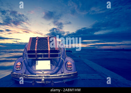 Retro car with luggage on the roof rack on the coastal road. Travel, vacation concepts.retro, vintage color Stock Photo