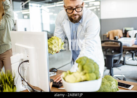 Senior nutritionist working on a diet plan or developing a new healthy product, at the working place with computer and fresh food in the office Stock Photo