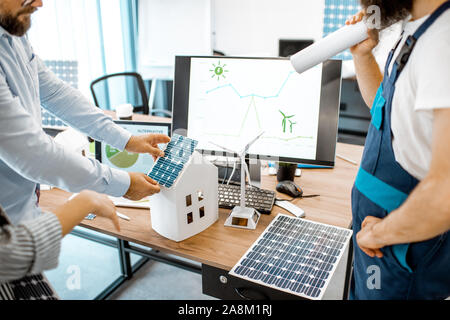 People working on a project of alternative energy, working with house model and computer in the office, close-up on the working place Stock Photo