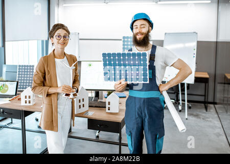 Portrait of a male worker and woman engineer working on a project of alternative energy, holding house model and solar panel in the office Stock Photo
