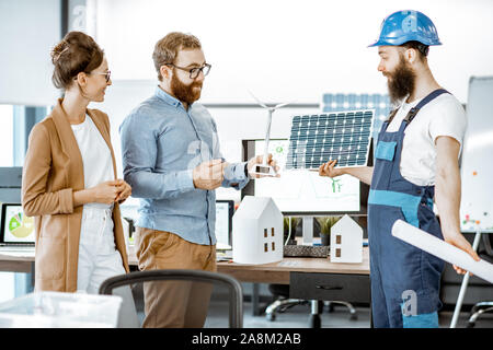 Young engineers and workman working on a project of alternative energy, holding house and wind turbine model in the office Stock Photo