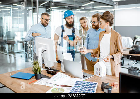 Group of engineers and workman working on a project of alternative energy at the office with computer, wind turbine and solar panels model Stock Photo