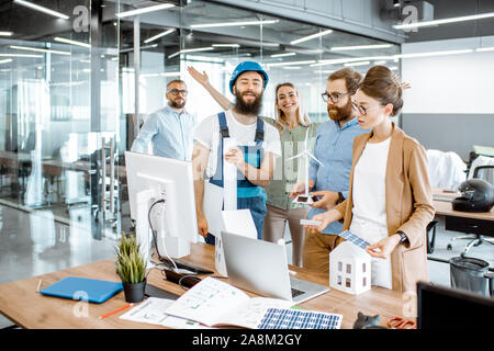 Group of engineers and workman working on a project of alternative energy at the office with computer, wind turbine and solar panels model Stock Photo