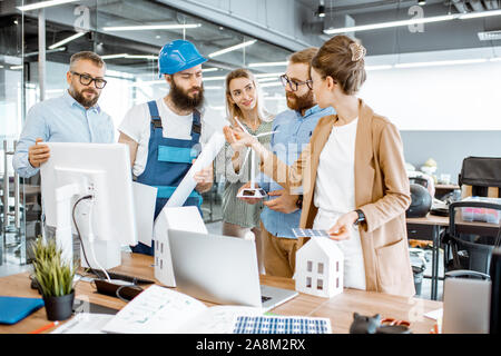 Group of engineers and workman working on a project of alternative energy at the office with computer, wind turbine and solar panels model Stock Photo