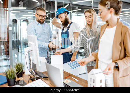 Group of engineers and workman working on a project of alternative energy at the office with computer, wind turbine and solar panels model Stock Photo
