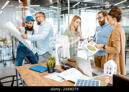 Group of young engineers working on a project of alternative energy, senior foreman and worker standing with blueprints in the office Stock Photo